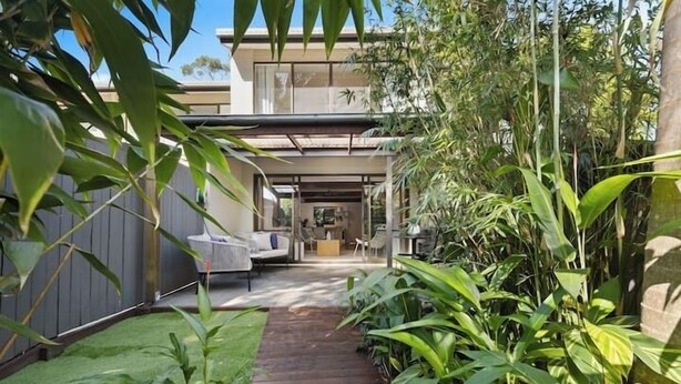A modern house with a wooden deck leading to a covered outdoor area.