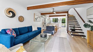 A modern living room with a blue sofa, a glass coffee table, and a staircase leading to an upper level.
