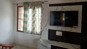 Una habitación con un televisor montado en una pared de mármol, una ventana con cortina y una silla de madera.