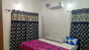 Un dormitorio con cama, cortinas, unidad de aire acondicionado y toma de corriente.