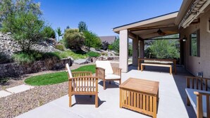An outdoor patio with wooden furniture, a covered seating area, and a view of a landscaped garden and rocky terrain. - *Gas Fireplace *Spacious *Family Friendly *Hot Tub (Prescott)