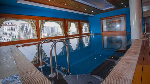 Une piscine intérieure moderne, dotée de grandes baies vitrées offrant une vue dégagée sur le paysage urbain.