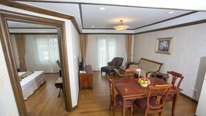 Une chambre d’hôtel avec un plancher en bois, une table à manger avec des chaises, un canapé, une télévision et un lit avec des rideaux.