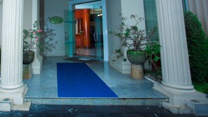 Une entrée d'immeuble avec un tapis bleu, des colonnes blanches et des plantes en pot.