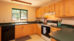 A kitchen with wooden cabinets, a dishwasher, a stove, and a window with a view of greenery. - ☀️🌲Falcons Perch: Nature Lover's Dream, in coastal hills above Blue Lake🪶 (Mckinleyville)