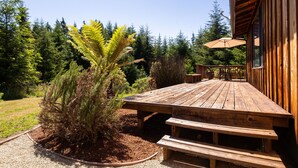 A wooden deck with benches and a table, surrounded by dense forest. - ☀️🌲Falcons Perch: Nature Lover's Dream, in coastal hills above Blue Lake🪶 (Mckinleyville)