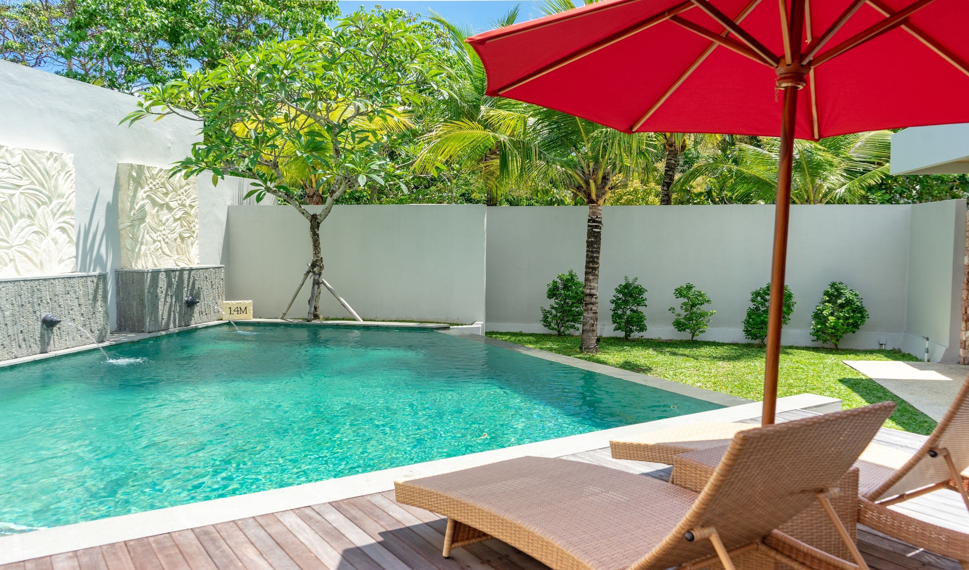 Una piscina con agua cristalina, rodeada por un muro blanco y abundante vegetación.
