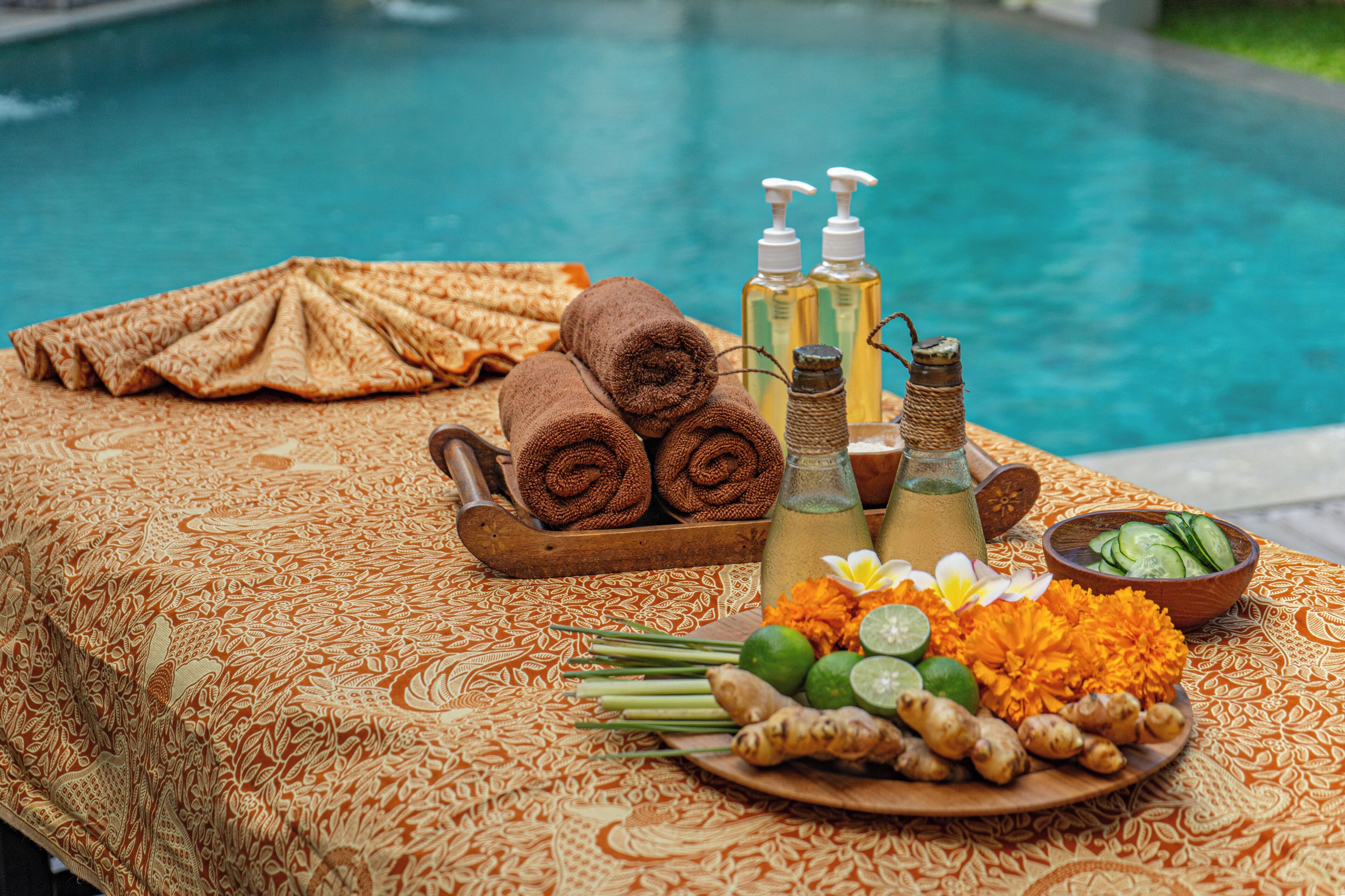 A table with towels, bottles, and a plate of ginger and flowers by a pool.