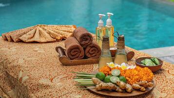 A table with towels, bottles, and a plate of ginger and flowers by a pool.