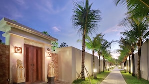 A pathway lined with palm trees and a building with a stone facade and wooden doors. - Vivara Bali Private Pool Villas & Spa Retreat (Jimbaran)