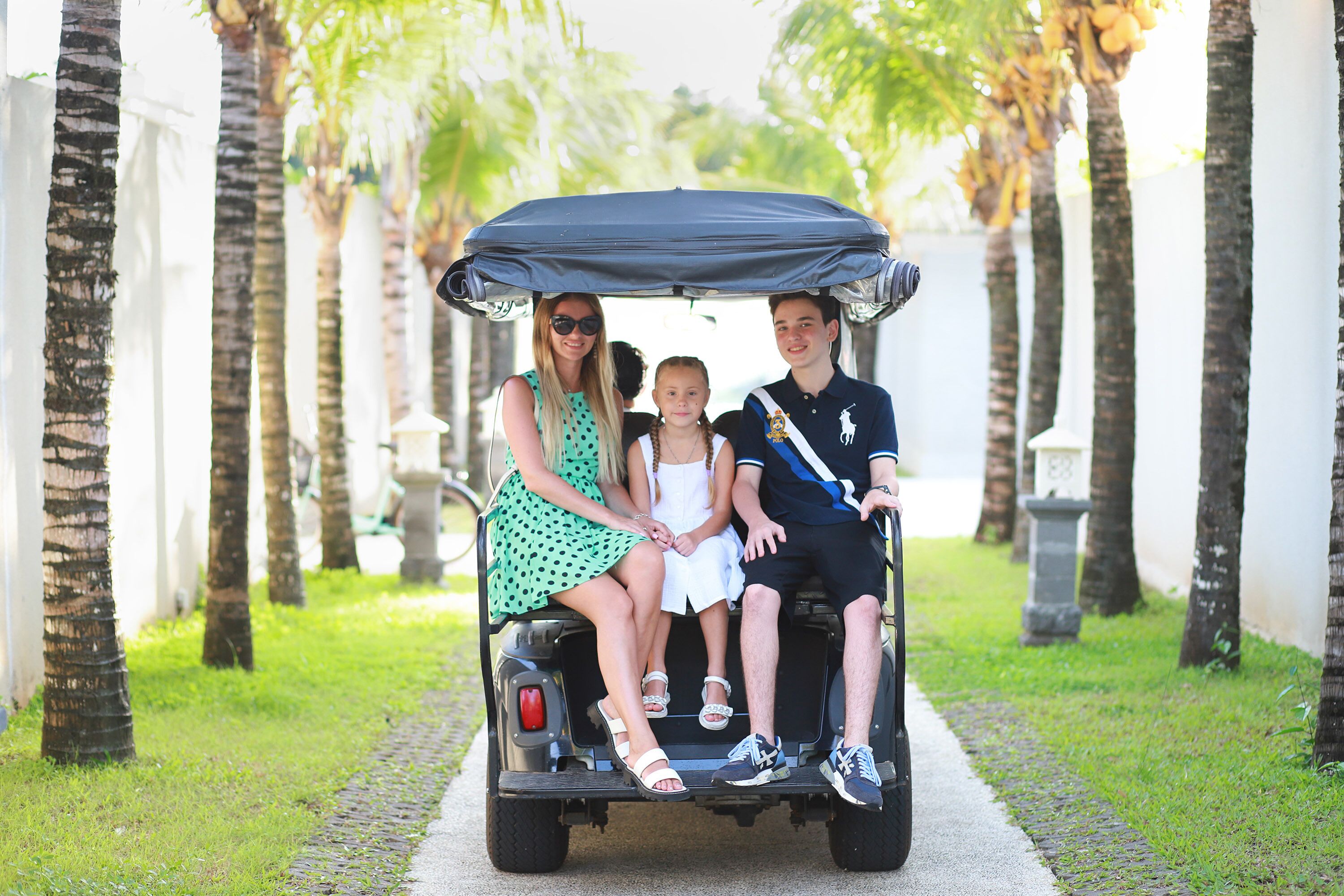 A family on a golf cart in a pathway lined with palm trees.