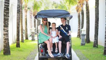 A family on a golf cart in a pathway lined with palm trees.