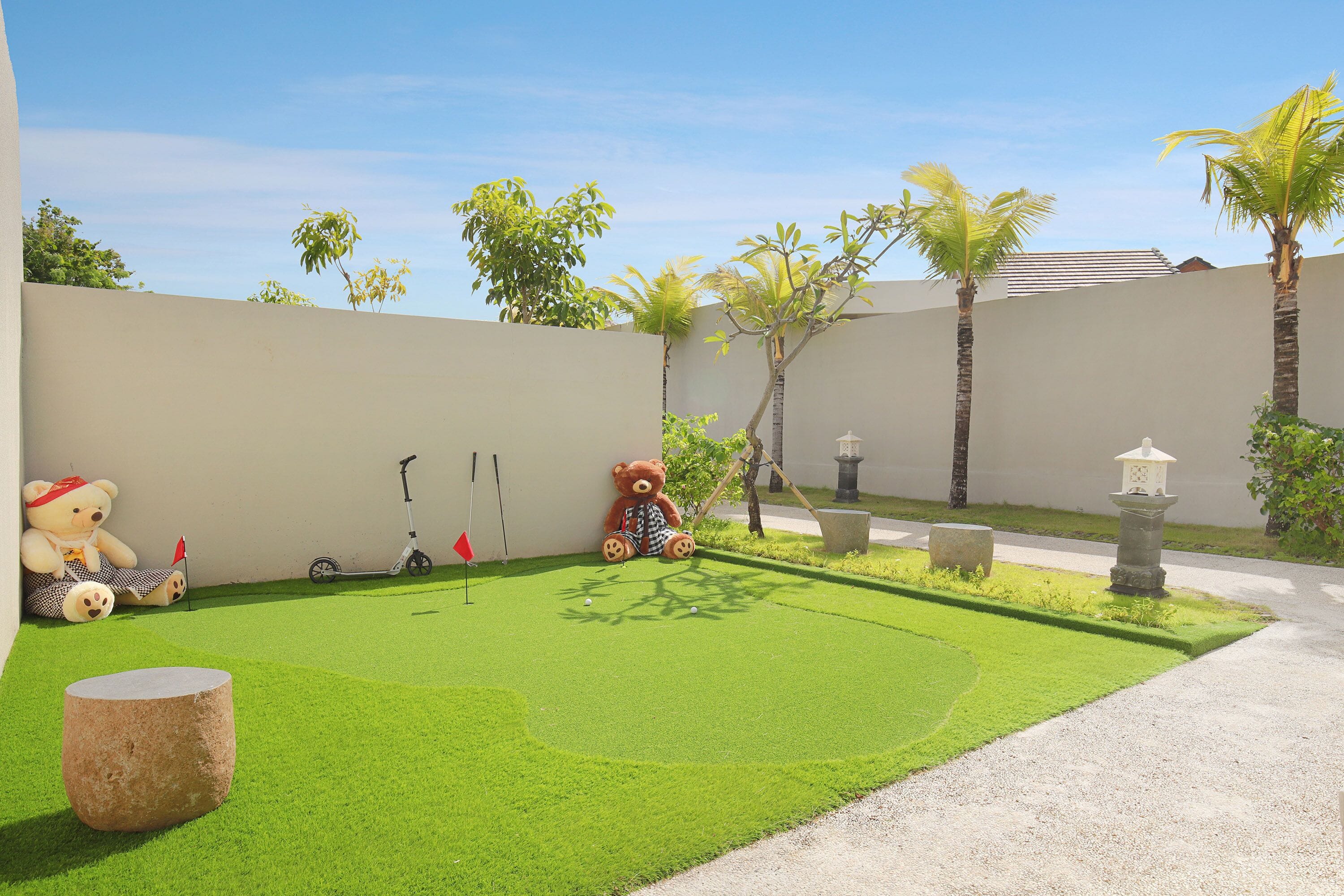 A well-maintained garden with artificial grass, a large teddy bear, a scooter, and a stone lantern.