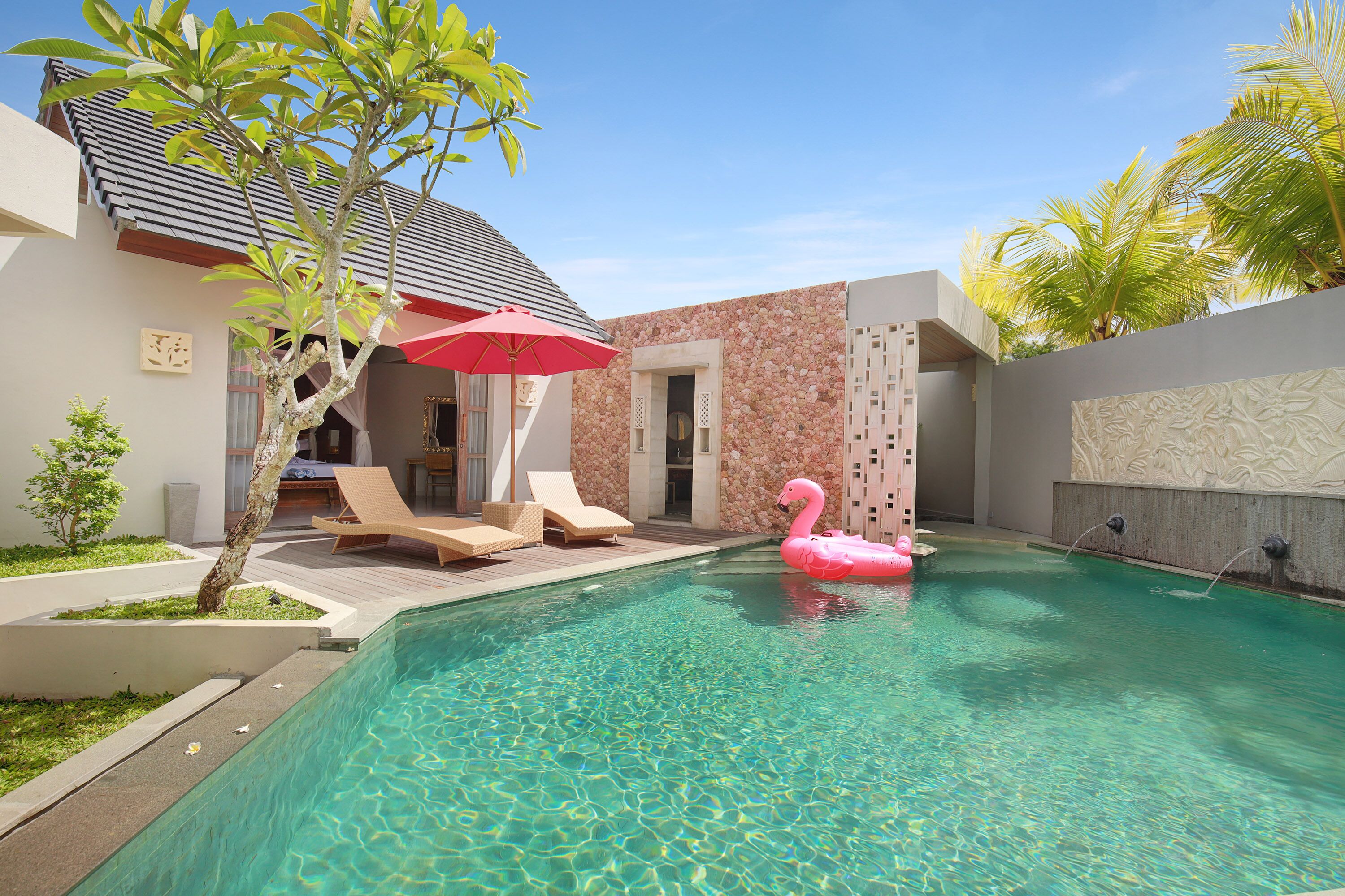 A swimming pool with a pink flamingo float, lounge chairs, and a red umbrella.