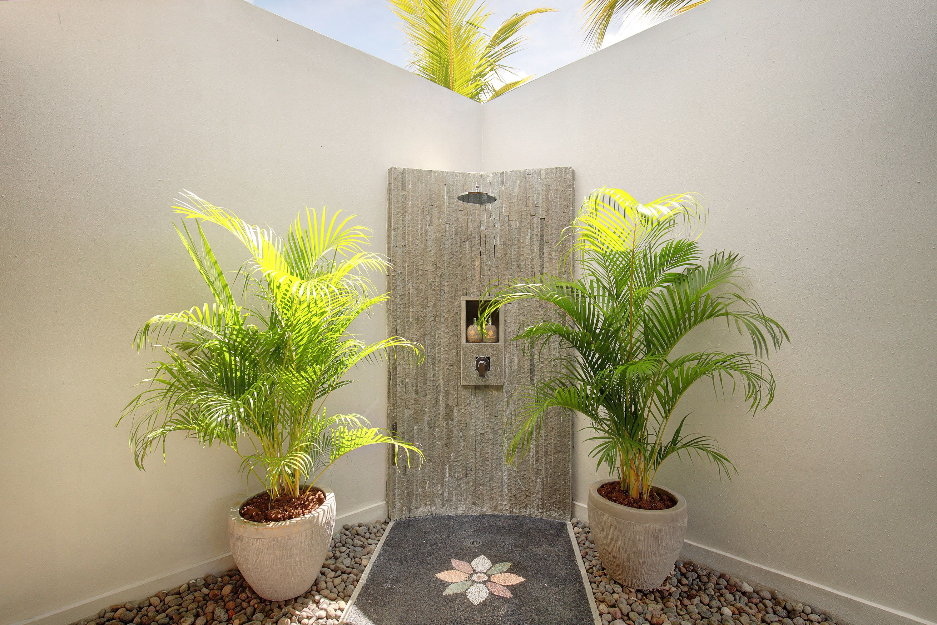 A shower area with a stone wall, potted plants, and a pebble pathway.