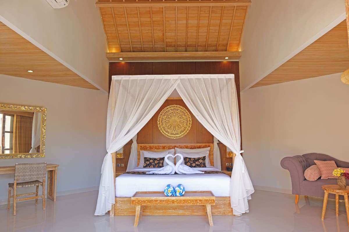 Un dormitorio con cama con dosel, cabecera de madera, espejo, mesita de noche y sofá.