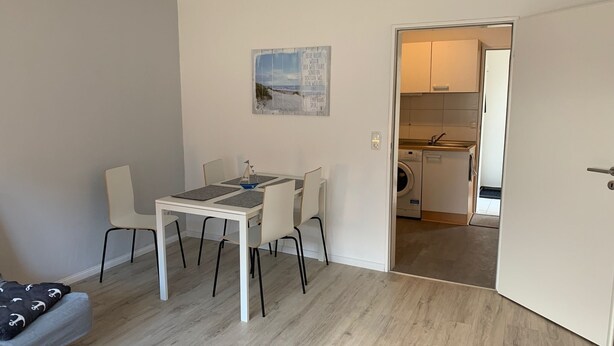 A compact living space with a dining area, a small kitchen, and a door leading to a laundry room. - Ferienwohnung Zwischen Lübeck und Travemünde (Lübeck)