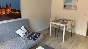 A modern living room with a grey sofa, a small table with four chairs, and a painting of a castle. - Ferienwohnung Zwischen Lübeck und Travemünde (Lübeck)