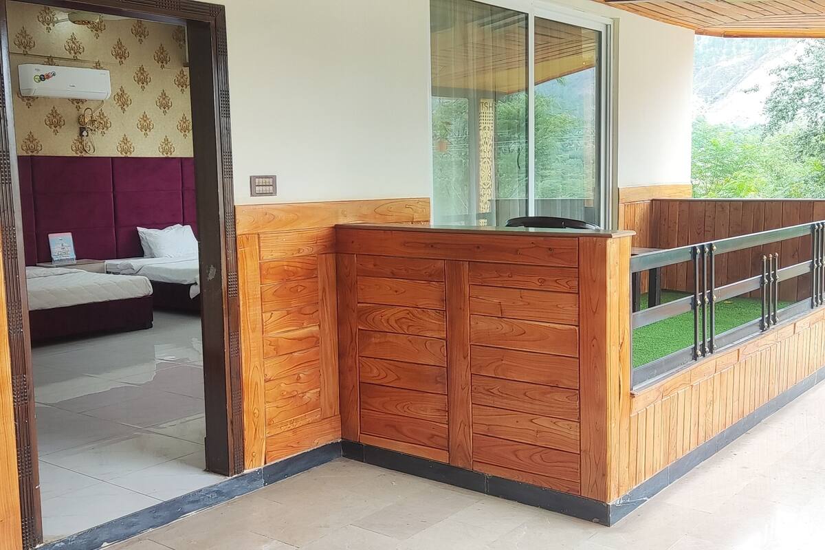 A hotel room with a wooden headboard, a bed with white linens, a wooden desk with drawers, and a window with a view of greenery.