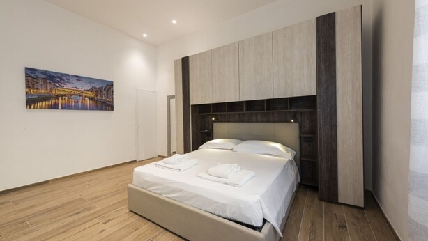 Quarto de hotel moderno com cama grande, piso de madeira, pintura de paisagem urbana na parede e painéis de madeira embutidos acima da cama.
