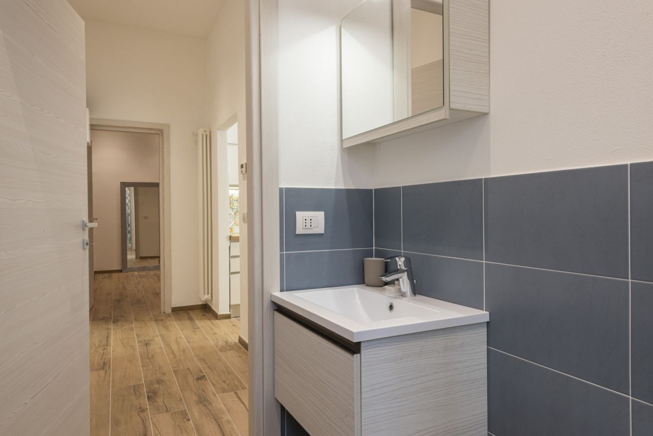 A modern bathroom with a white sink, dark blue tiles, and a mirror above the sink.