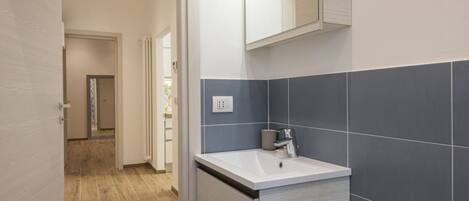 A modern bathroom with a white sink, dark blue tiles, and a mirror above the sink.