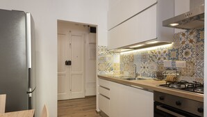 Cozinha com armários brancos, geladeira de aço inoxidável, painel de azulejos e bancada de madeira.