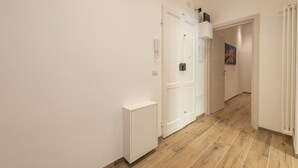 Um corredor com paredes brancas, um radiador, uma porta e um quadro na parede.