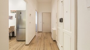 Um corredor com piso de madeira, uma geladeira de aço inoxidável e uma porta branca.