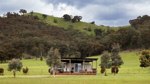 A secluded cabin with a covered porch, surrounded by a lush green landscape and hills.