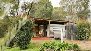 Un chalet rustique doté d’un porche en bois, d’un espace extérieur couvert aménagé en salon et d’un jardin planté de plantes tropicales.