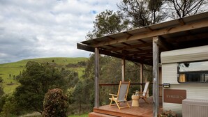 Une remorque aménagée en camping-car, dotée d’une terrasse en bois, d’un chevalet et d ’une chaise.