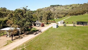 Une propriété rurale, accessible par un chemin de terre, avec une maison entourée d’arbres et donnant sur des champs ouverts.