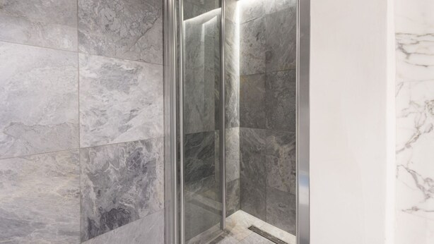 A modern bathroom with marble tiles, a glass shower enclosure, and a visible drain. - Santo Spirito View in Florence by Mmega (Firenze)