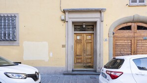 A narrow street with a yellow building, a wooden double door entrance, and two parked cars. - Santo Spirito View in Florence by Mmega (Firenze)