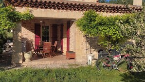 A stone building with a tiled roof, a wooden table and chairs outside, and a bicycle parked nearby.