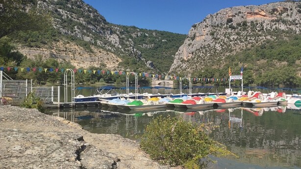 A marina with boats docked, surrounded by rocky hills and greenery.