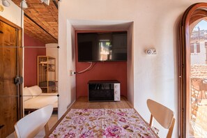 A compact room with a TV mounted on the wall, a microwave, a floral tablecloth, and a wooden ceiling.