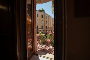 Een balkon met rode stoelen en een tafeltje, met uitzicht op een straat met gebouwen.