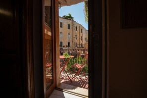 A balcony with red chairs and a small table, overlooking a street with buildings.
