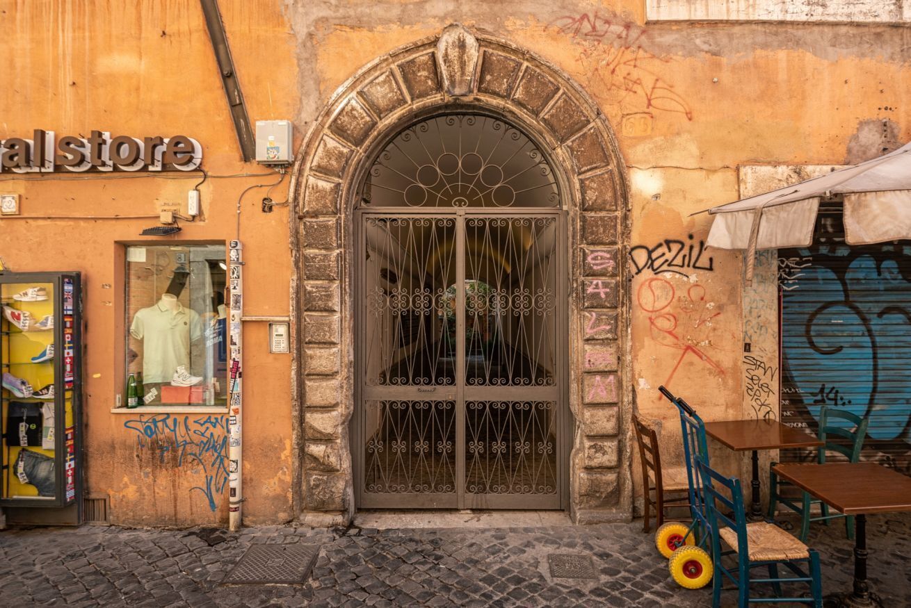 A storefront with a metal gate, a mannequin in the window, and graffiti on the wall.