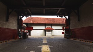 An indoor entrance with a tiled floor, a directional arrow, and a building with a red-tiled roof in the background.