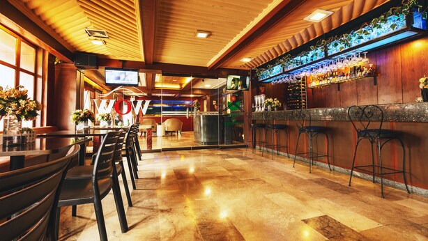 A bar area with wooden ceiling, bar stools, and a counter with bottles.