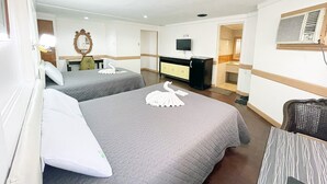 A hotel room with two beds, a desk, a television, and a bathroom.