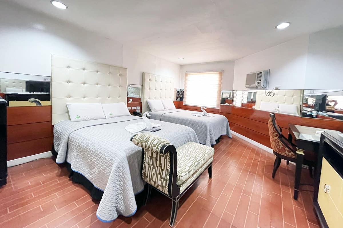 A hotel room with two beds, a small seating area, a desk, and a mirror.