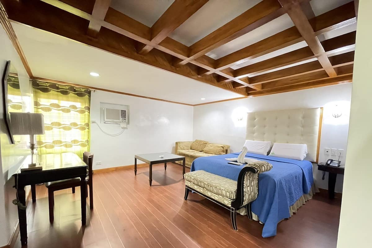 A hotel room with a bed, a sofa, a small table, and a desk.