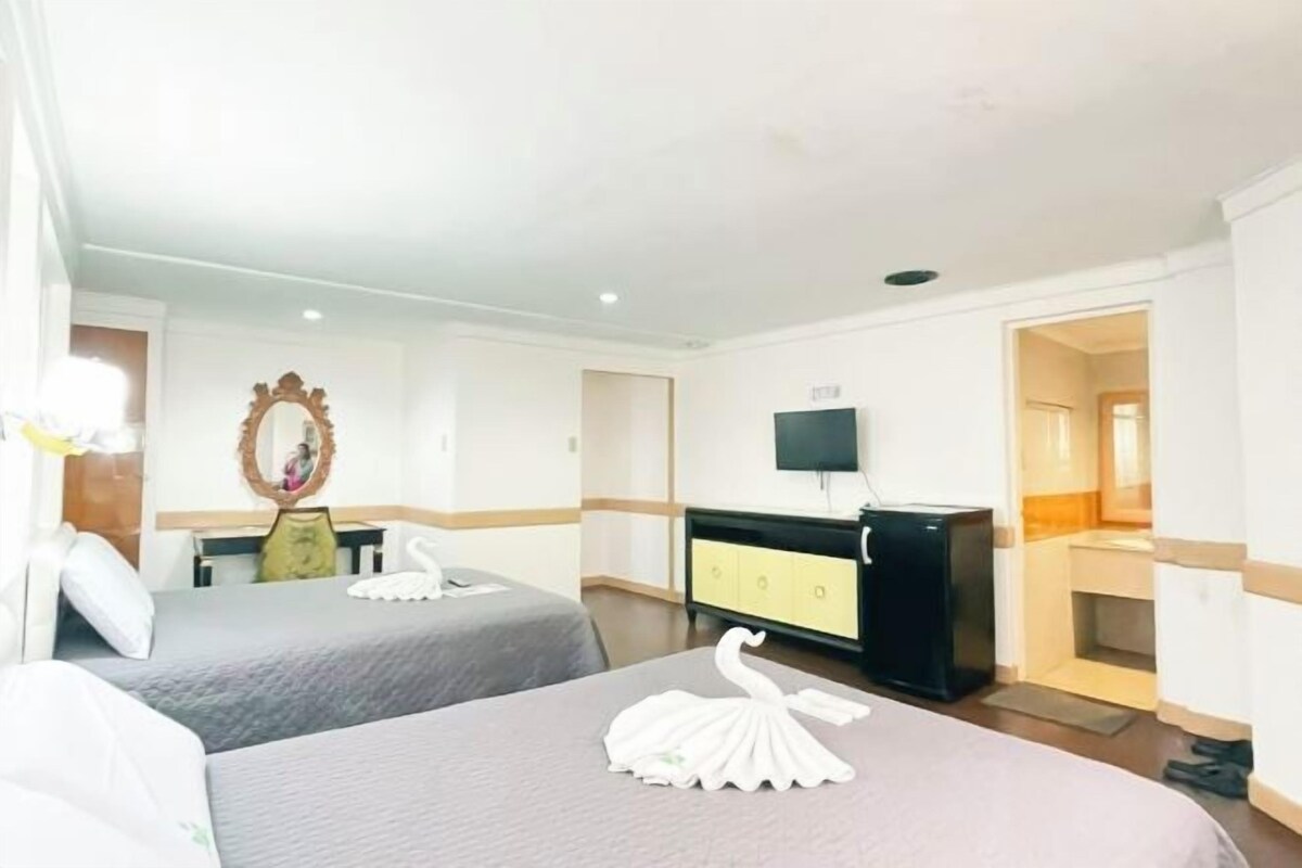 A hotel room with two beds, a dresser, a mirror, and a television.