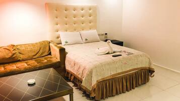 A hotel room with a large bed, a sofa, a small table, and a nightstand.