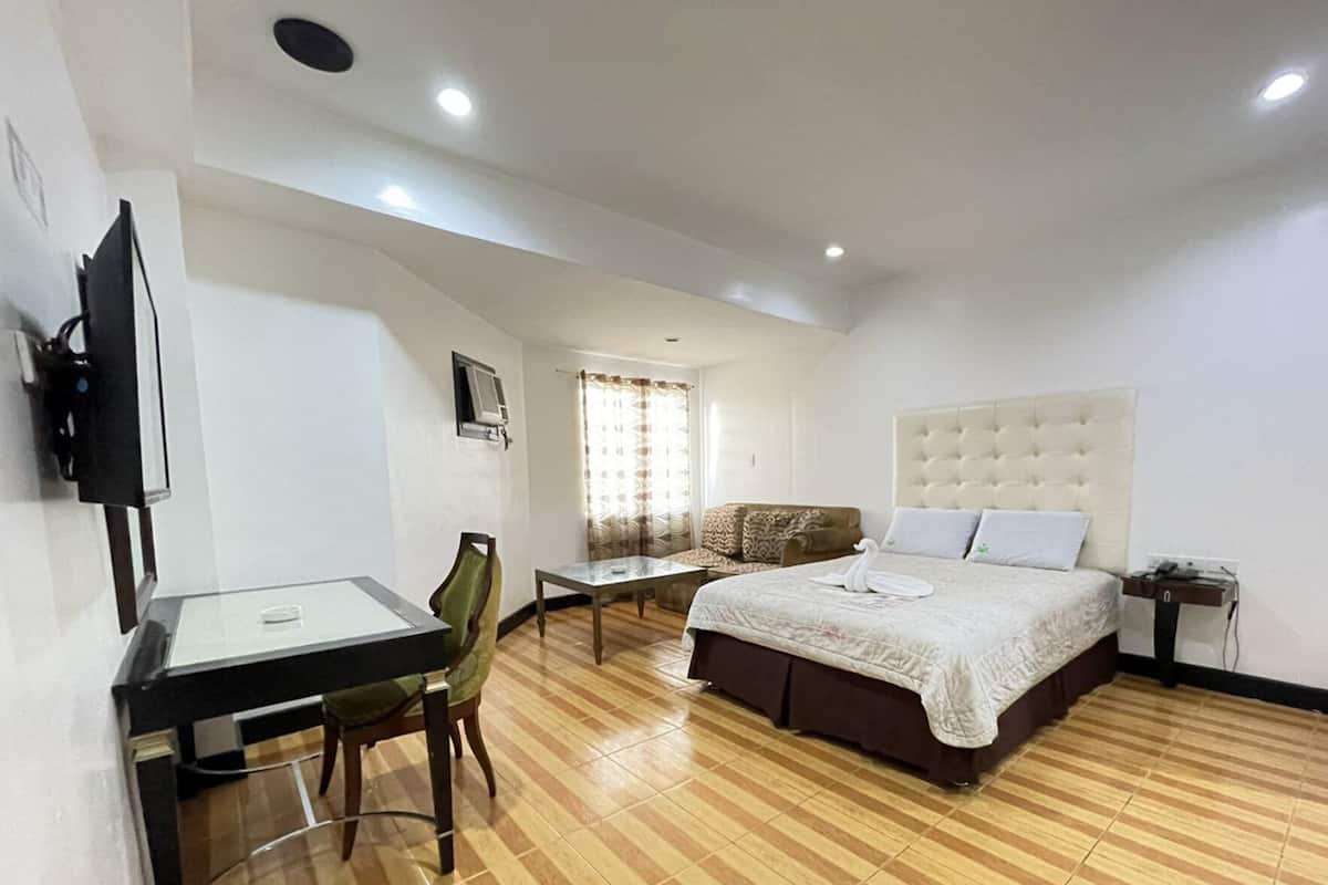 A bedroom with a bed, a desk, a chair, a TV, and a window with curtains.