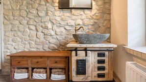A stone wall with a mirror, a wooden cabinet with drawers, and a bowl sink.